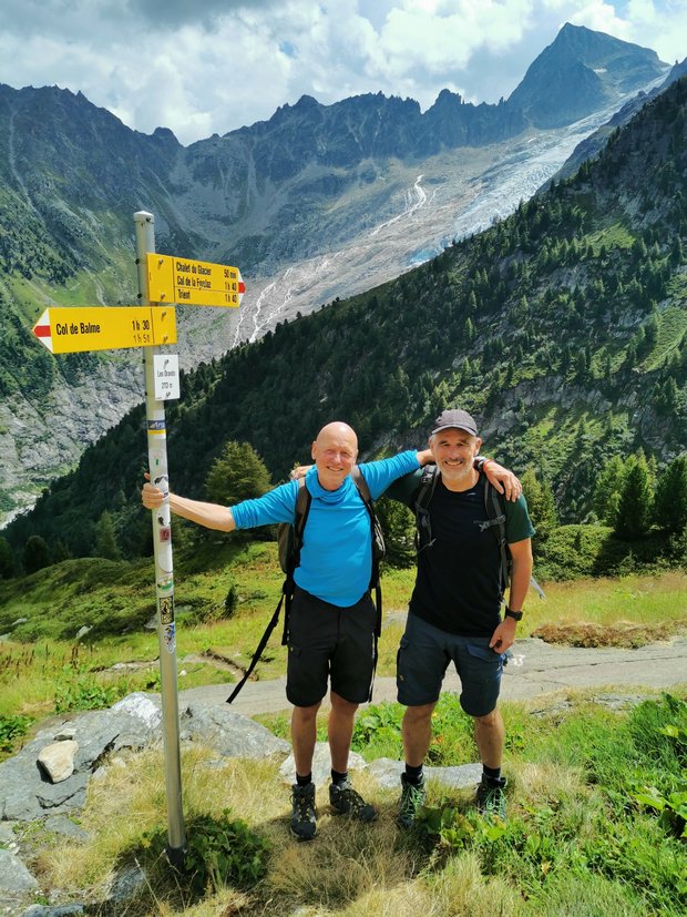 Manno und Stefan 2022 Stefan und Manno stehen an einem Wegweiser vor Bergpanorama